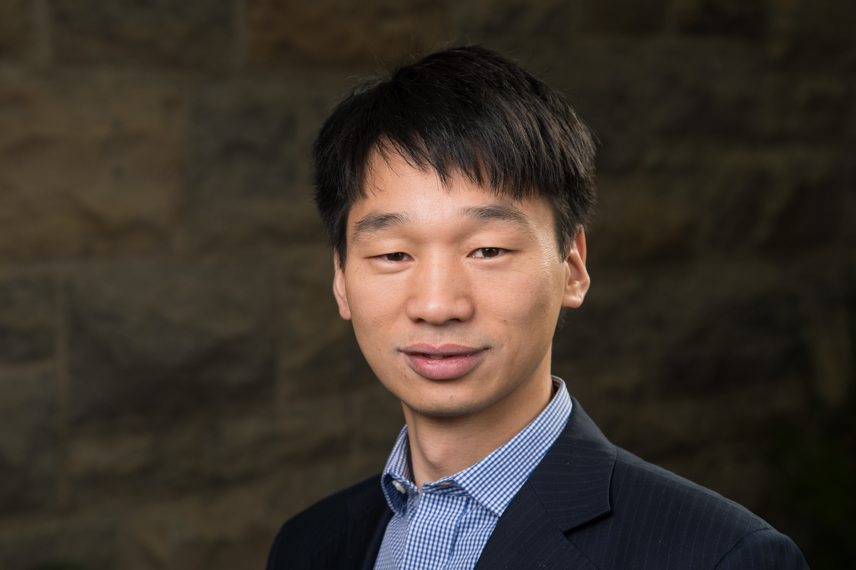 Virginia Tech chemist Guoliang “Greg” Liu stands in front of a Hokie Stone wall, wearing a blazer and dress shirt.
